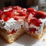 A close-up view of a moist slice of Strawberry Shortcake Sheet Cake topped with whipped cream and fresh strawberries.