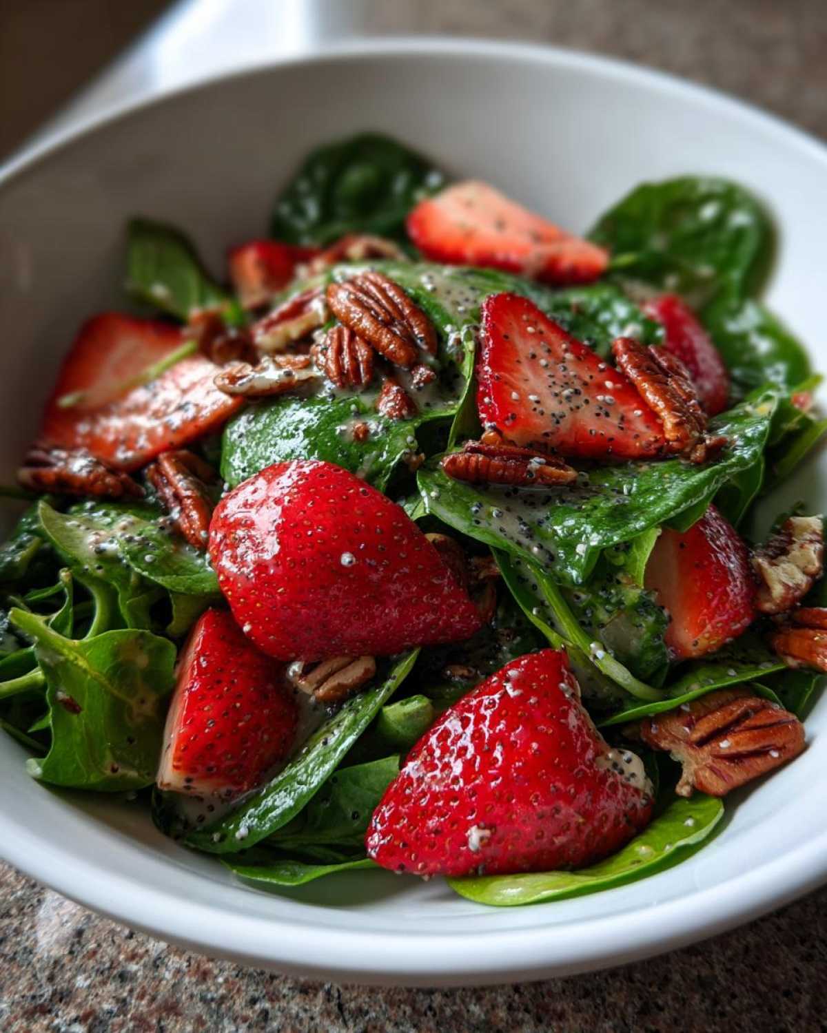Close-up of a vibrant Strawberry Spinach Salad with pecans and creamy poppy seed dressing.