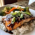 Close-up of a Teriyaki Salmon Rice Bowl featuring a glazed salmon fillet over white rice with broccoli and carrots.