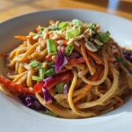 A close-up of creamy Thai Peanut Noodles with Crunchy Veggies, topped with peanuts and green onions.