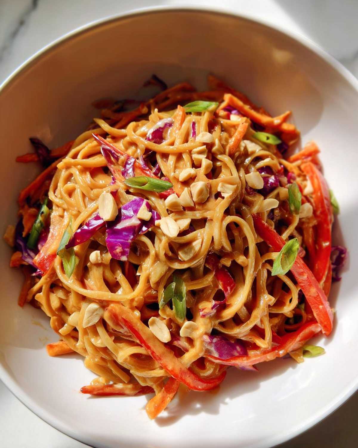 A close-up of Thai Peanut Noodles with Crunchy Veggies, coated in peanut sauce and topped with chopped peanuts.