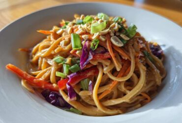 A close-up of creamy Thai Peanut Noodles with Crunchy Veggies, topped with peanuts and green onions.
