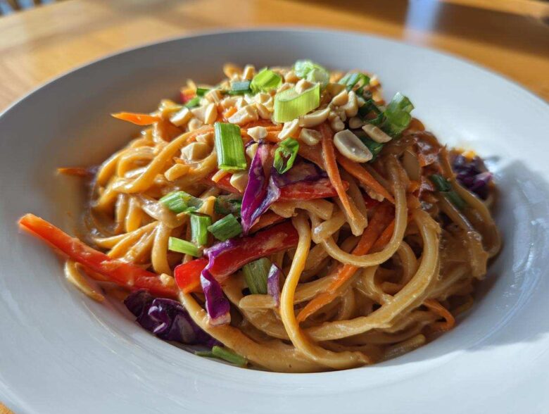 A close-up of creamy Thai Peanut Noodles with Crunchy Veggies, topped with peanuts and green onions.