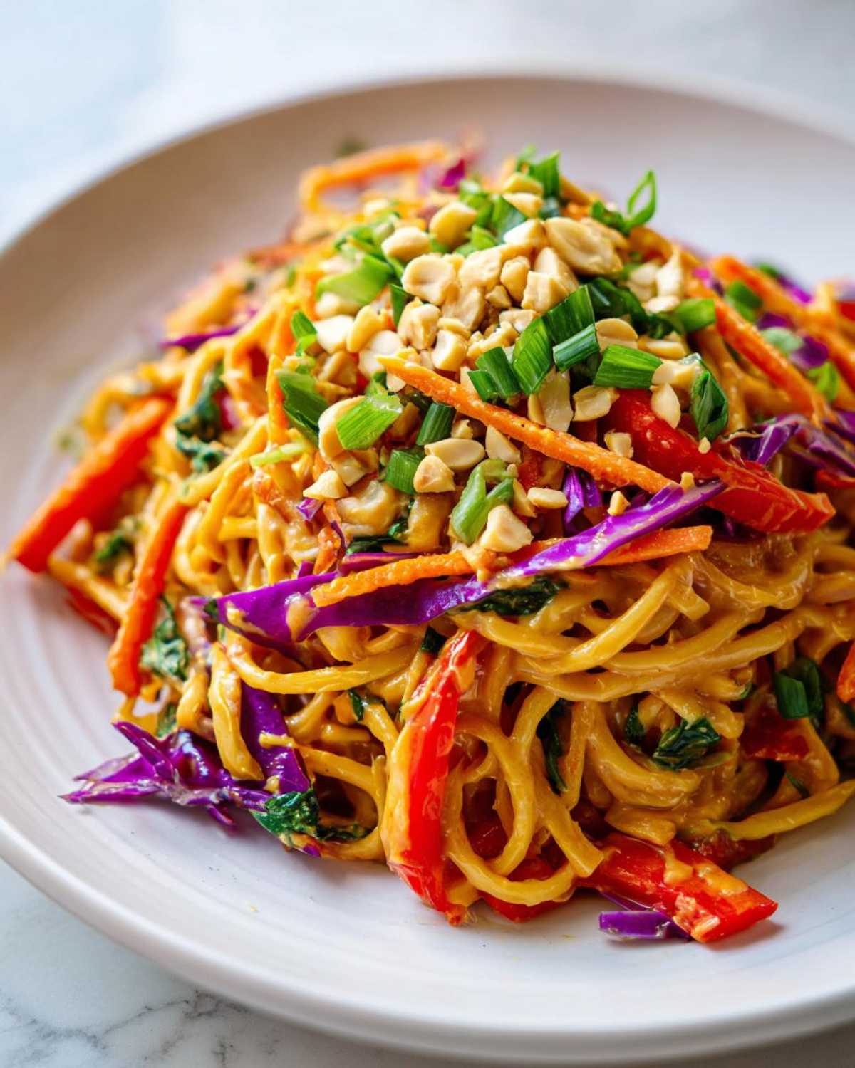 Close-up of creamy Thai Peanut Noodles with crunchy red cabbage, carrots, and topped with chopped peanuts and scallions.