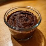 A close-up of rich, dark Vegan Chocolate Avocado Mousse served in a small clear glass dish on a wooden surface.