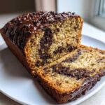 A loaf of Vegan Chocolate Banana Bread, sliced to show the marbled chocolate interior and chocolate chip topping.