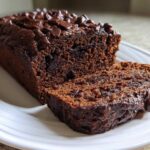 A loaf of moist Vegan Chocolate Banana Bread, partially sliced, topped with melted chocolate chips.