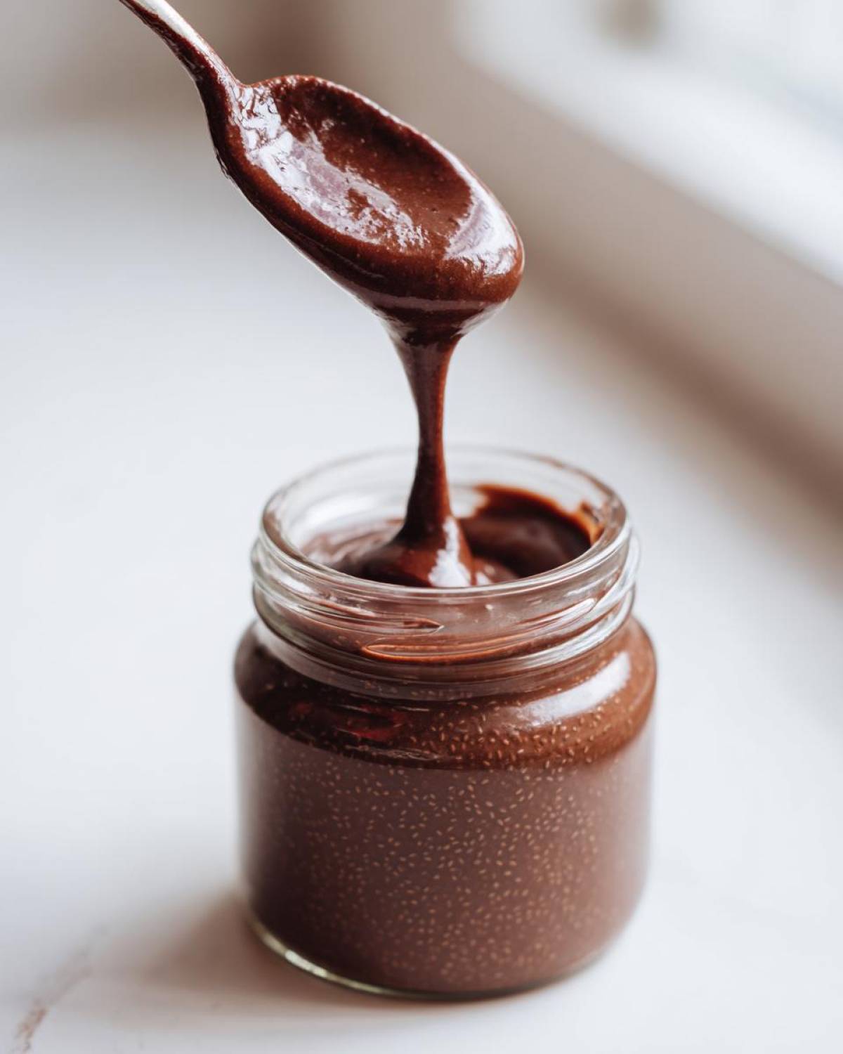 A spoonful of thick Vegan Chocolate Chia Pudding is dripping back into a glass jar.