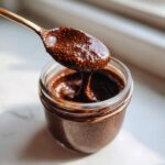 A golden spoon lifting thick Vegan Chocolate Chia Pudding from a small glass jar.
