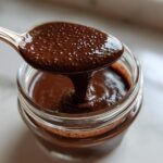A spoonful of thick, dark Vegan Chocolate Chia Pudding being lifted from a small glass jar.