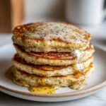 Close-up of a stack of fluffy Vegan Lemon Poppy Seed Pancakes drizzled with a thick lemon glaze.