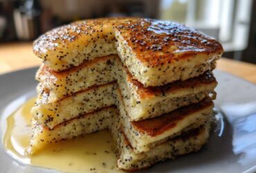 A tall stack of fluffy Vegan Lemon Poppy Seed Pancakes drizzled with lemon syrup.