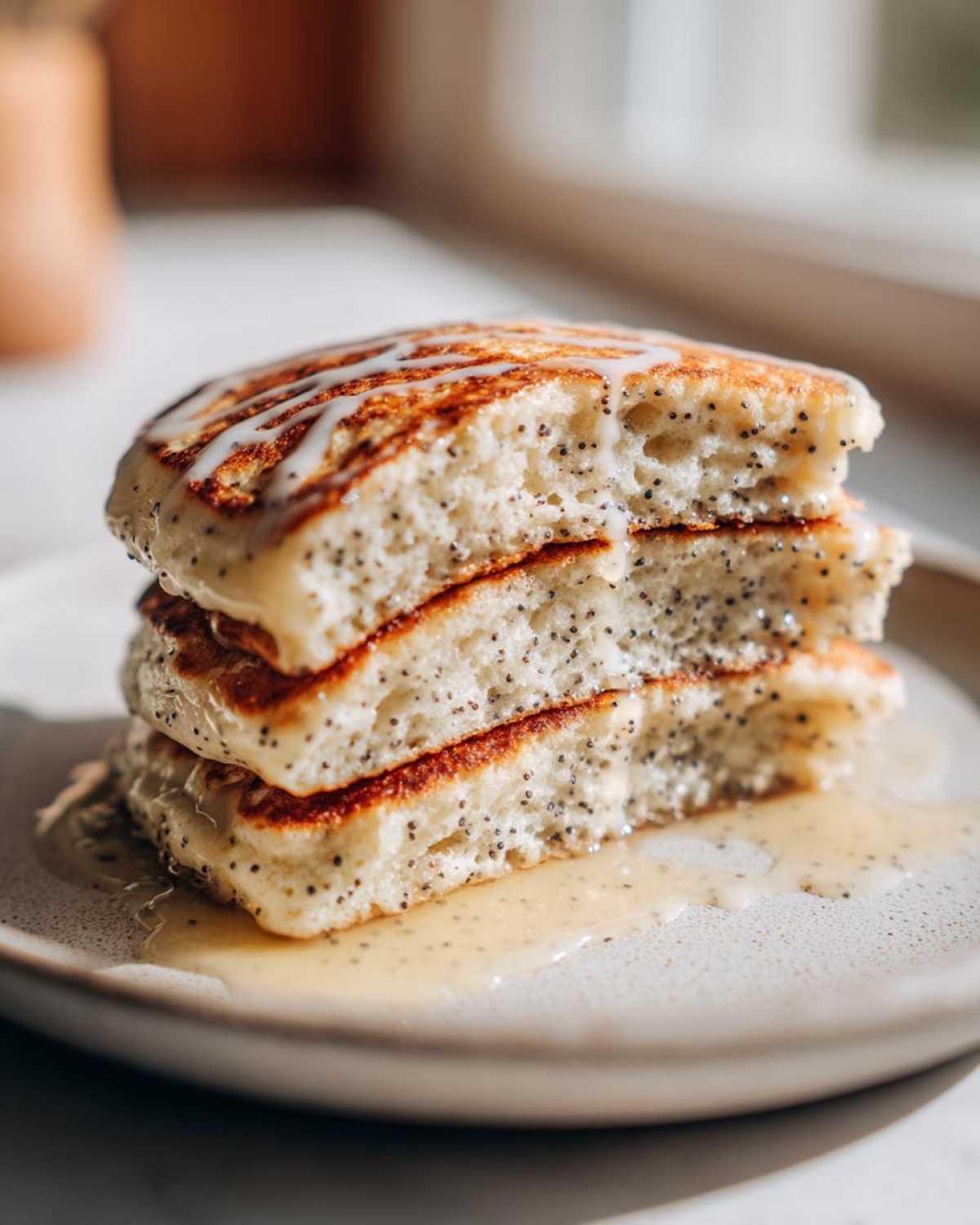 Close-up of a stack of three fluffy Vegan Lemon Poppy Seed Pancakes drizzled with glaze and syrup.