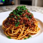 A close-up of spaghetti topped generously with rich Vegan Lentil Bolognese and fresh parsley.