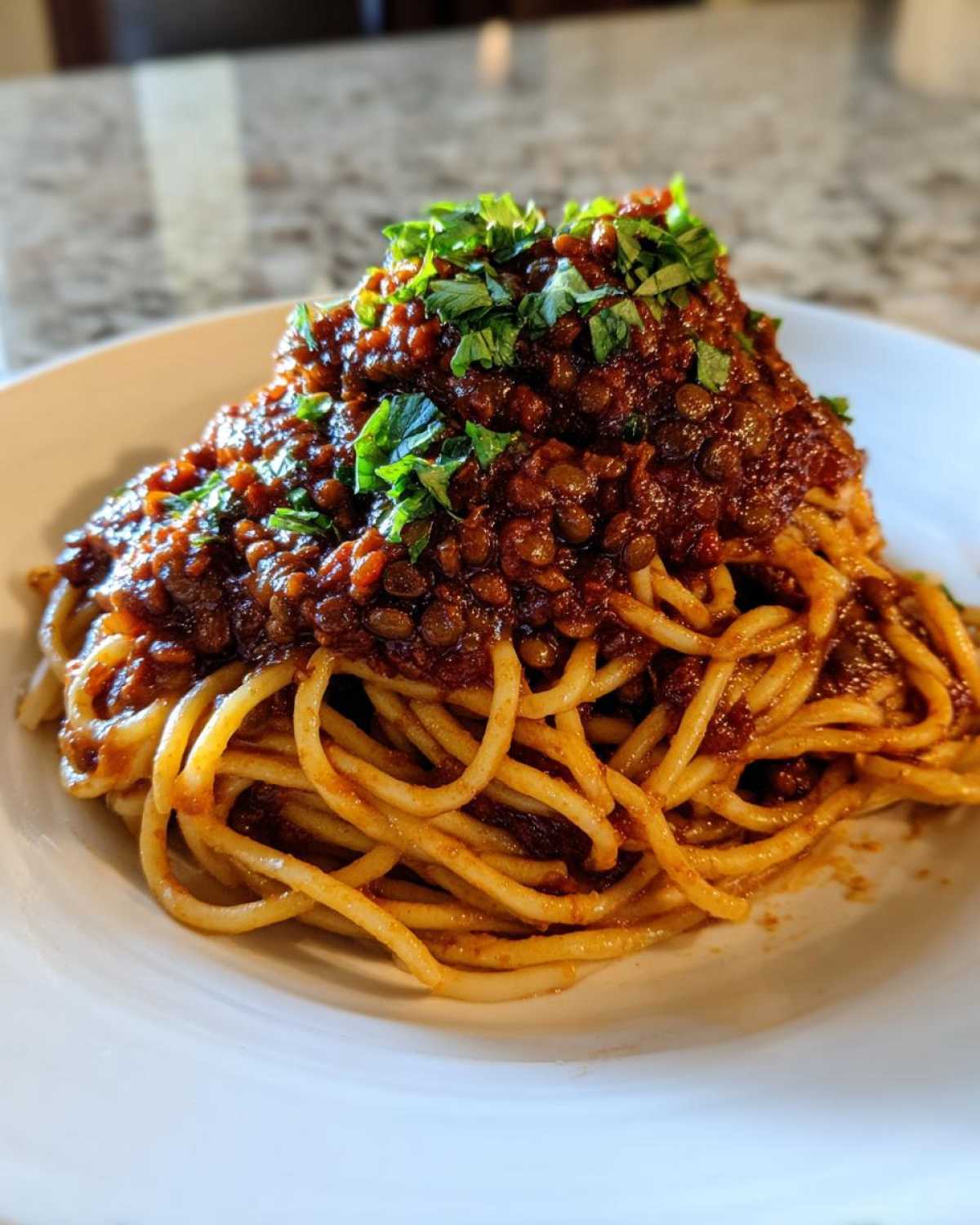 Close-up of spaghetti topped generously with rich Vegan Lentil Bolognese sauce and fresh parsley.