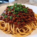 A close-up of a serving of rich Vegan Lentil Bolognese sauce generously spooned over a bed of spaghetti, topped with fresh parsley.