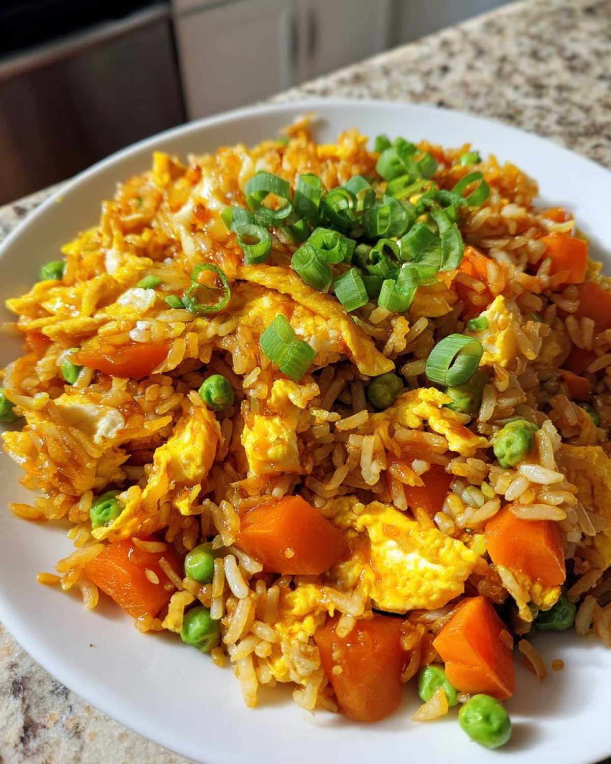 A close-up of a serving of Vegetable Fried Rice with scrambled egg, bright orange carrots, green peas, topped with fresh scallions.