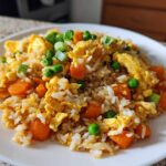 Close-up of a plate of Vegetable Fried Rice with scrambled egg, bright orange carrots, and green peas.