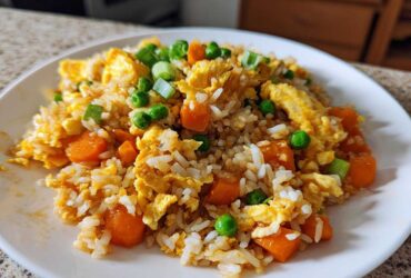 Close-up of a plate of Vegetable Fried Rice with scrambled egg, bright orange carrots, and green peas.
