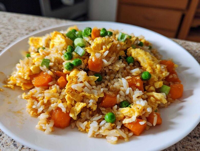 Close-up of a plate of Vegetable Fried Rice with scrambled egg, bright orange carrots, and green peas.