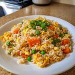 A plate of Vegetable Fried Rice with scrambled egg, bright orange carrots, green peas, and scallions garnish.