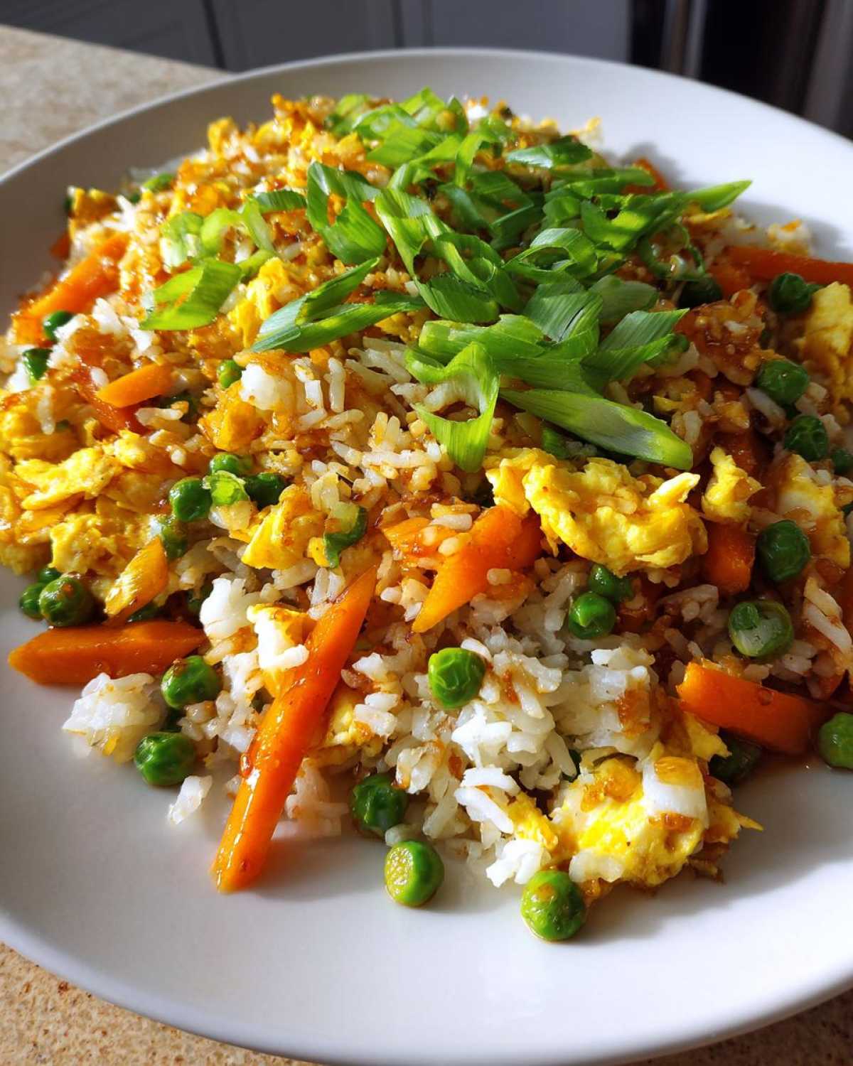 A close-up of a serving of Vegetable Fried Rice with peas, carrots, scrambled egg, topped with fresh green onions.