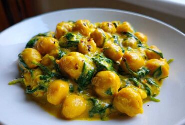 Close-up of a serving of Vegetarian Chickpea Curry with Coconut Milk, featuring yellow chickpeas and wilted spinach in a creamy sauce.