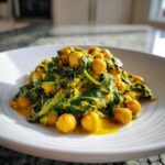 A serving of vibrant Vegetarian Chickpea Curry with coconut milk sauce and wilted spinach on a white plate.