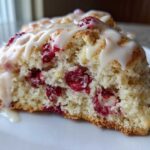Close-up of a flaky White Chocolate Raspberry Scones half showing bright red berries and white chocolate chunks inside, topped with glaze.