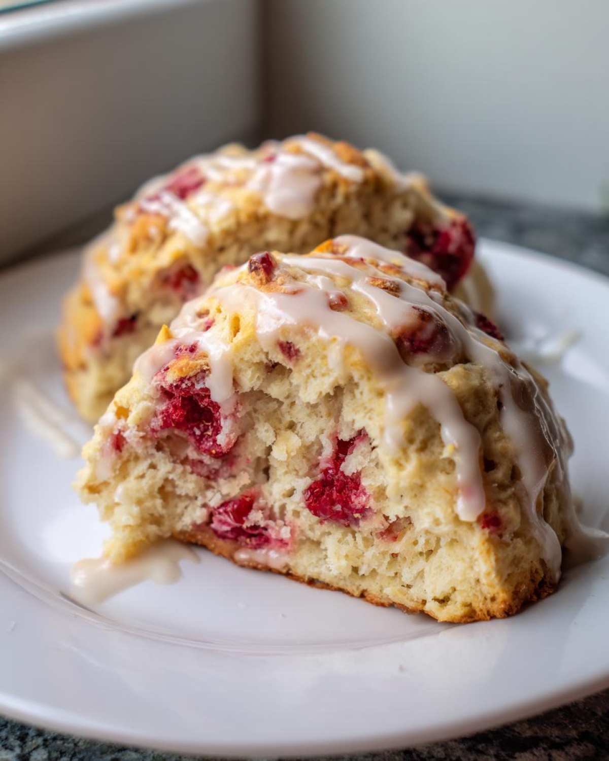 Close-up of a flaky White Chocolate Raspberry Scones, cut in half, showing raspberries and drizzled with white glaze.