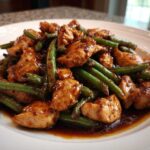 Close-up of glazed chicken pieces mixed with vibrant green beans, served in a rich sauce, highlighting the chicken and green beans dinner.