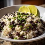 A close-up of a white bowl filled with fluffy white rice mixed with black beans, topped with fresh cilantro, served with lime wedges. Perfect beans and rice.