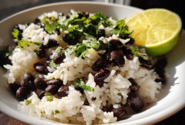 Close-up of a bowl of fluffy white rice mixed with black beans, topped with fresh cilantro and a lime wedge, showcasing the beans and rice dish.