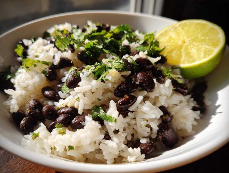 Close-up of a bowl of fluffy white rice mixed with black beans, topped with fresh cilantro and a lime wedge, showcasing the beans and rice dish.