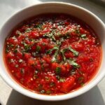 Close-up of a vibrant, chunky tomato sauce topped with fresh, chopped basil leaves.