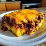 A hearty slice of tamale pie featuring a thick cornbread base topped with seasoned ground meat and melted cheddar cheese.