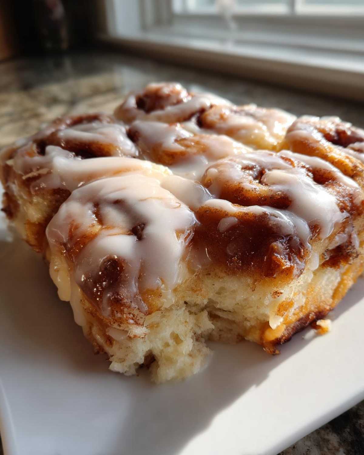 Close-up of a portion of soft, baked cinnamon roll casserole covered in thick white icing.