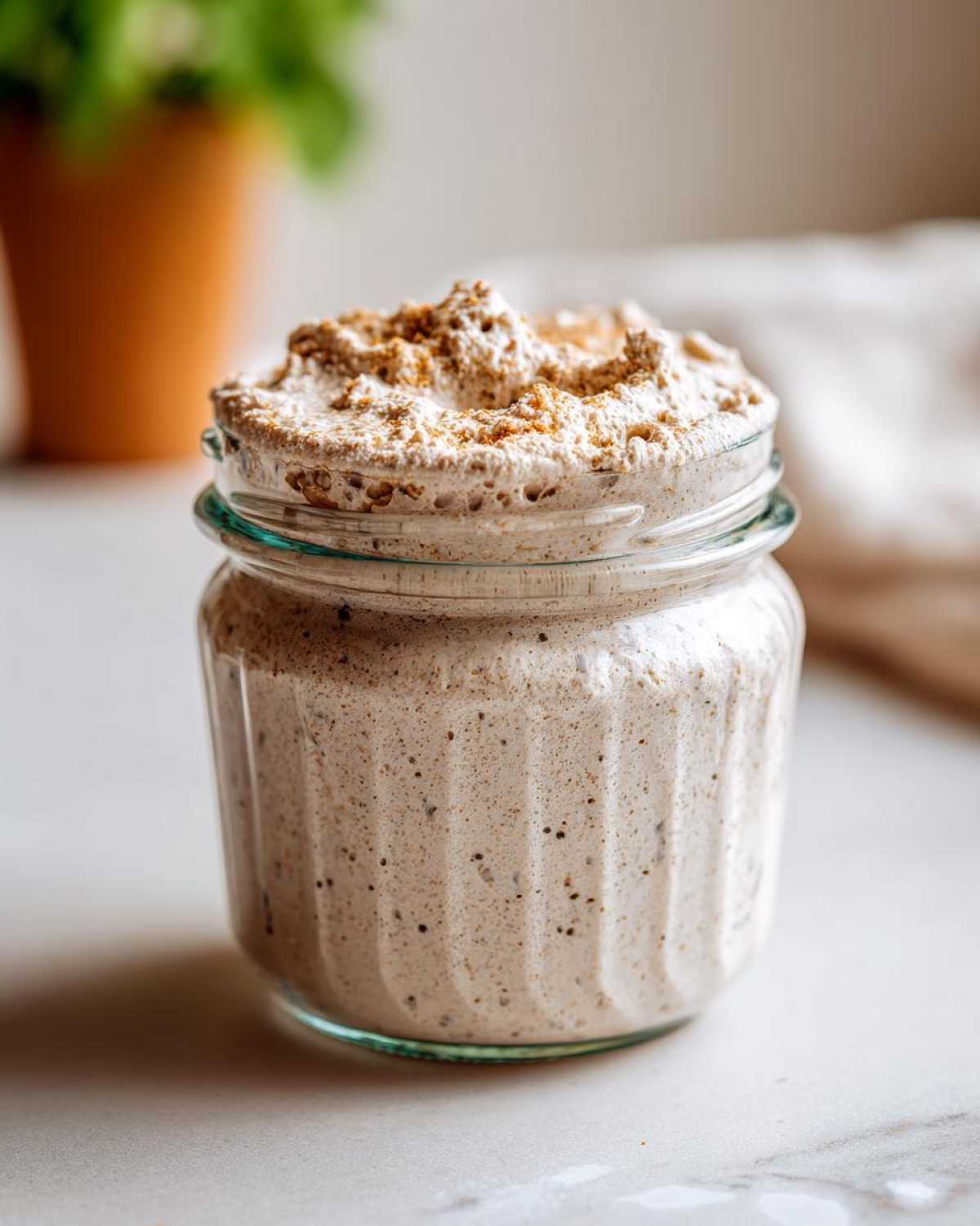 A bubbly, active sourdough starter overflowing slightly from a clear glass jar, showing aeration.