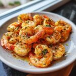A plate of perfectly cooked, seasoned air fryer frozen shrimp glistening with butter and herbs.
