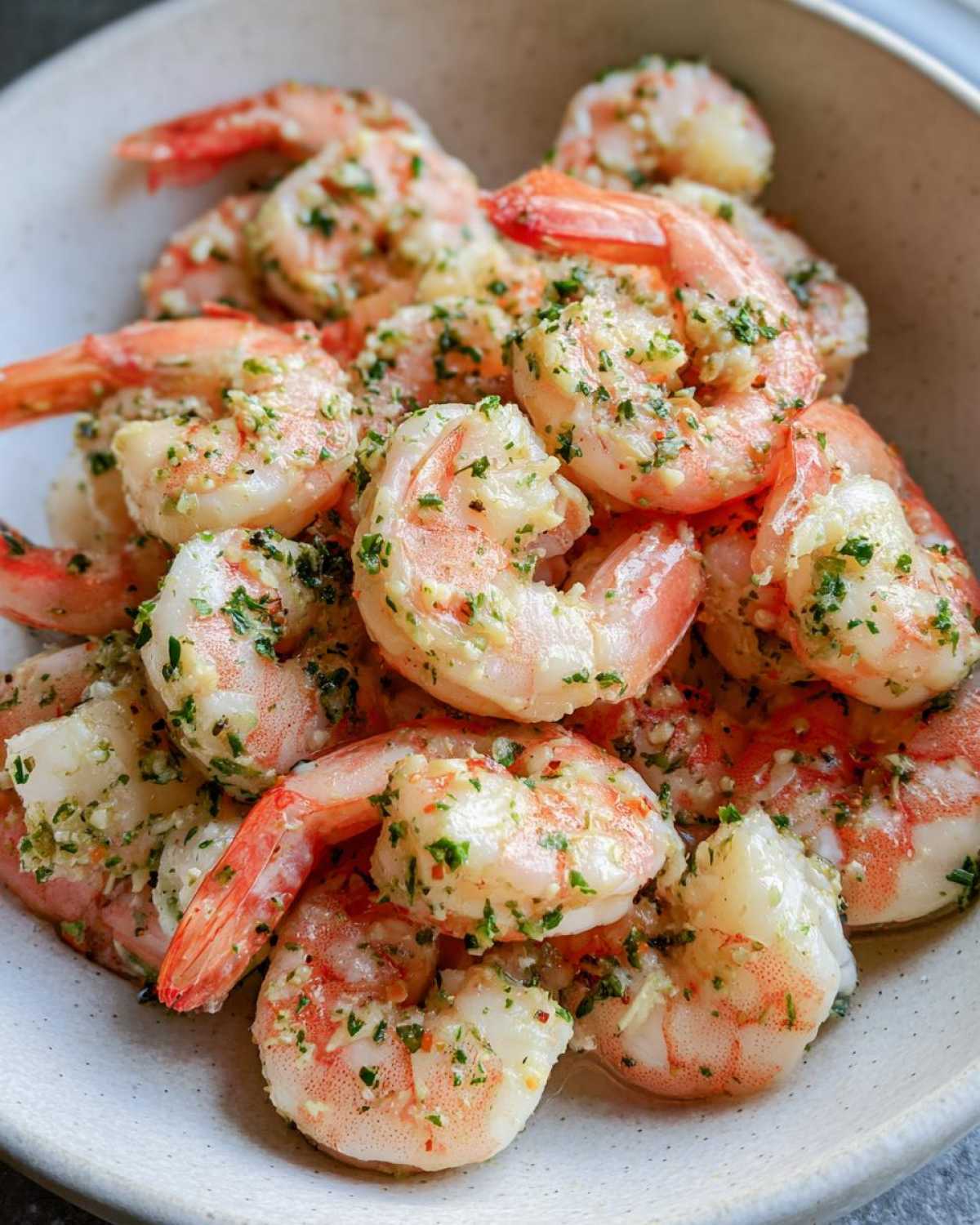 Close-up of cooked air fryer frozen shrimp tossed in garlic butter and parsley, served in a light-colored bowl.