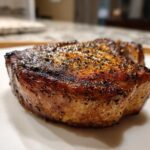 Close-up of a thick, juicy air fryer pork chop with a dark, seasoned crust.