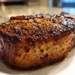 Close-up of a thick, juicy air fryer pork chop with a dark, caramelized, seasoned crust.