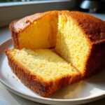 A close-up of a slice cut from a golden brown olive oil cake, showing its moist, yellow crumb.