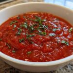 Close-up of rich, chunky tomato sauce topped with fresh basil in a white serving bowl.