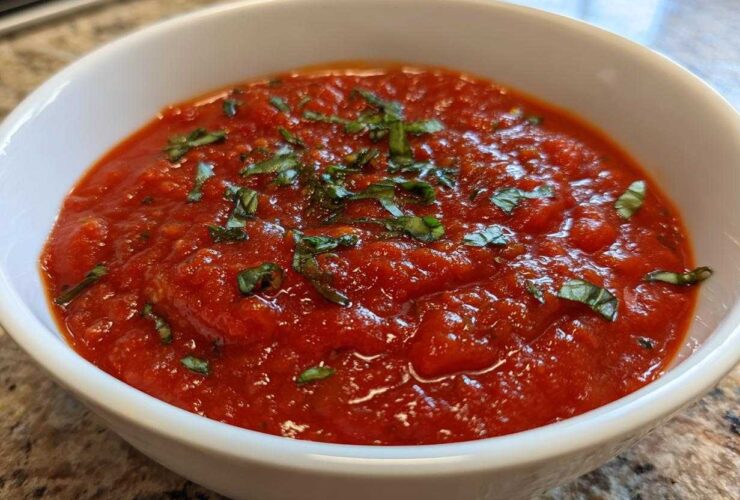 Close-up of rich, chunky tomato sauce topped with fresh basil in a white serving bowl.