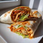 Cross-section view of an amazing buffalo chicken wrap filled with shredded chicken, lettuce, and carrots.