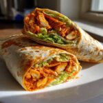 Two halves of an amazing buffalo chicken wrap, showing spicy chicken, lettuce, and carrots inside a tortilla.