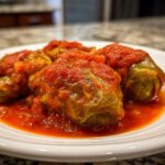 Close-up of three savory cabbage rolls smothered in rich, bright red tomato sauce on a white plate.