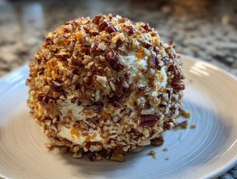 A perfectly formed, creamy cheese ball recipe coated entirely in chopped pecans, resting on a white plate.