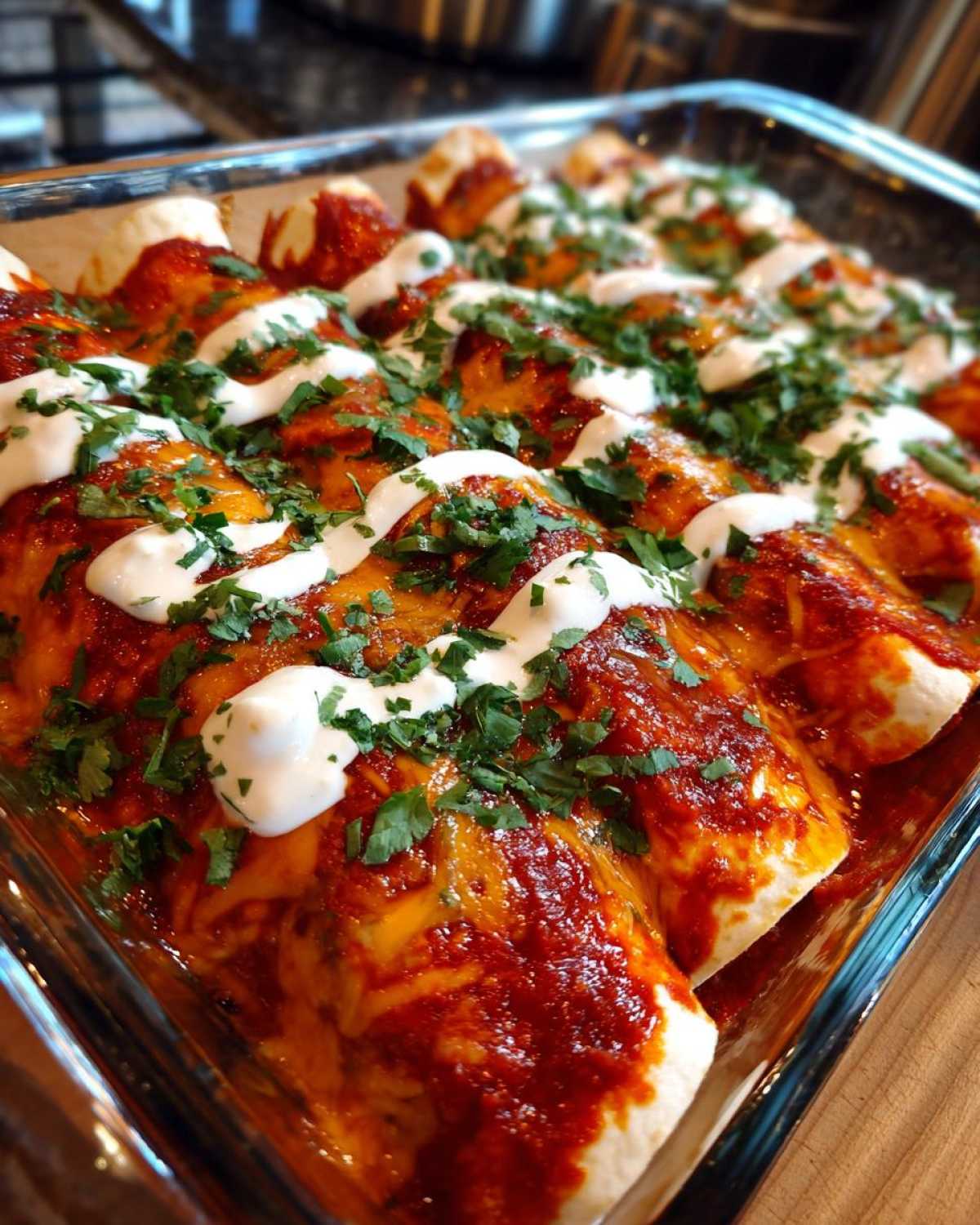 A glass baking dish filled with freshly baked cheese enchiladas covered in red sauce, melted cheese, sour cream, and cilantro.